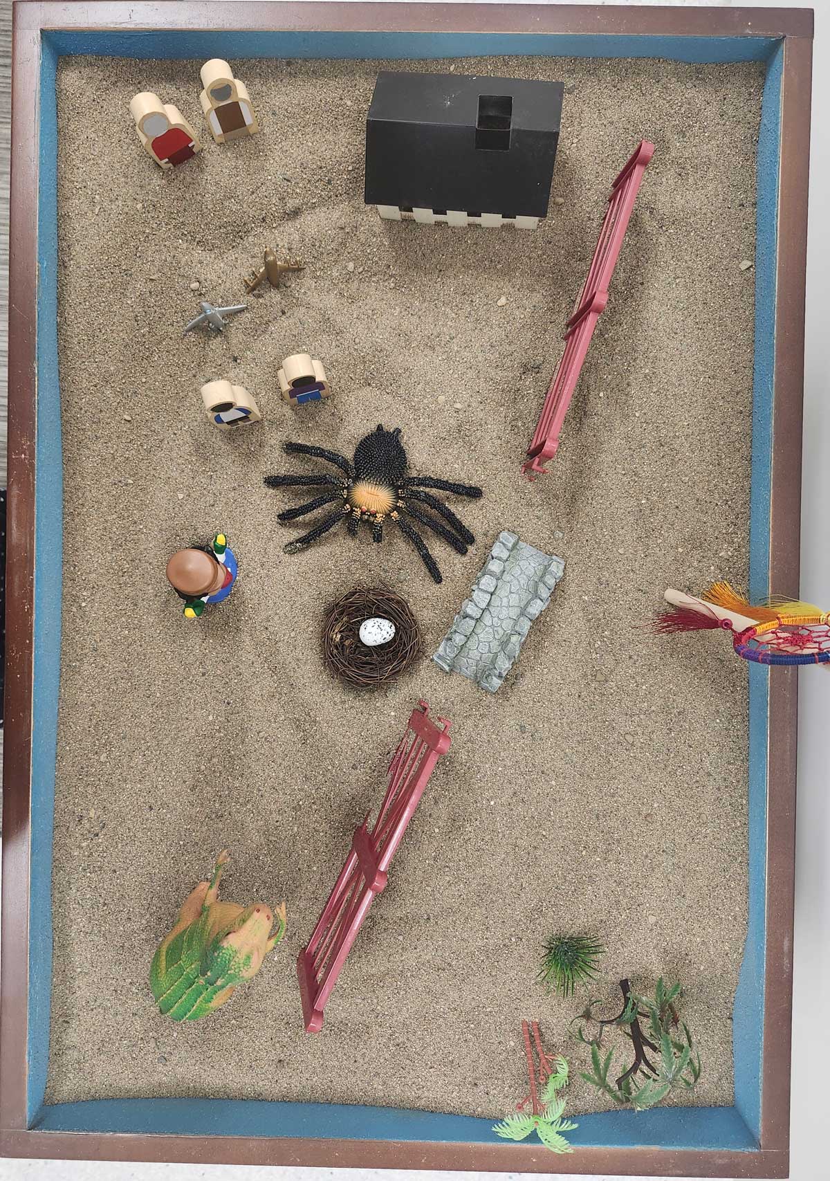 An overhead view of a therapeutic sand tray featuring a mix of miniature objects used for exploring the Third Space.