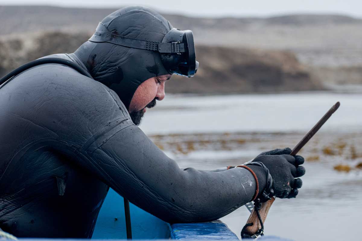 A fisher-diver in full suit neoprene praying on a small boat before plunging into the cold ocean.