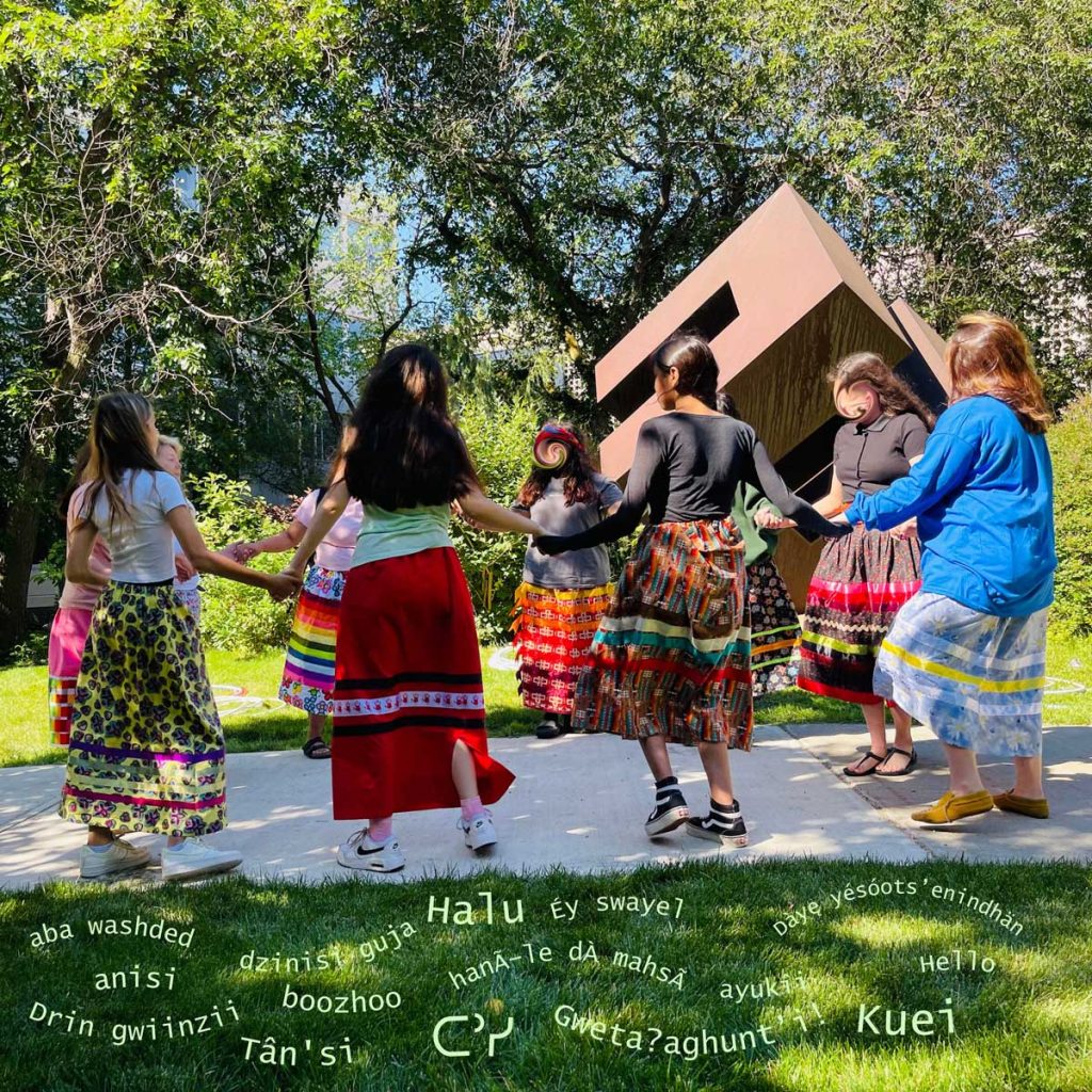 Outdoor round dance by youths in traditional skirts for Indigenous language revitalization, with greeting words overlaid.