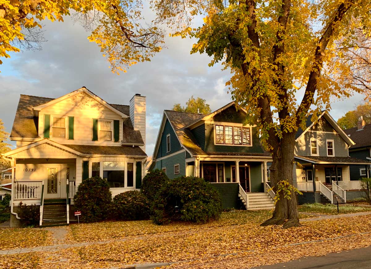 Three large heritage homes, surrounded by autumn leaves, framed by elm trees, and bathed in warm late-afternoon light.