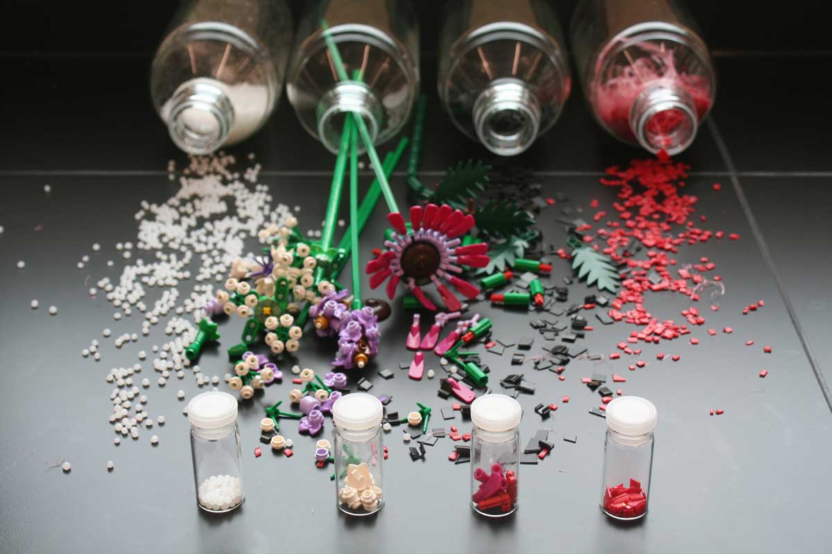 Colourful microplastics and plastic flowers spill from four large jars. In front, four plastic samples are contained in vials.