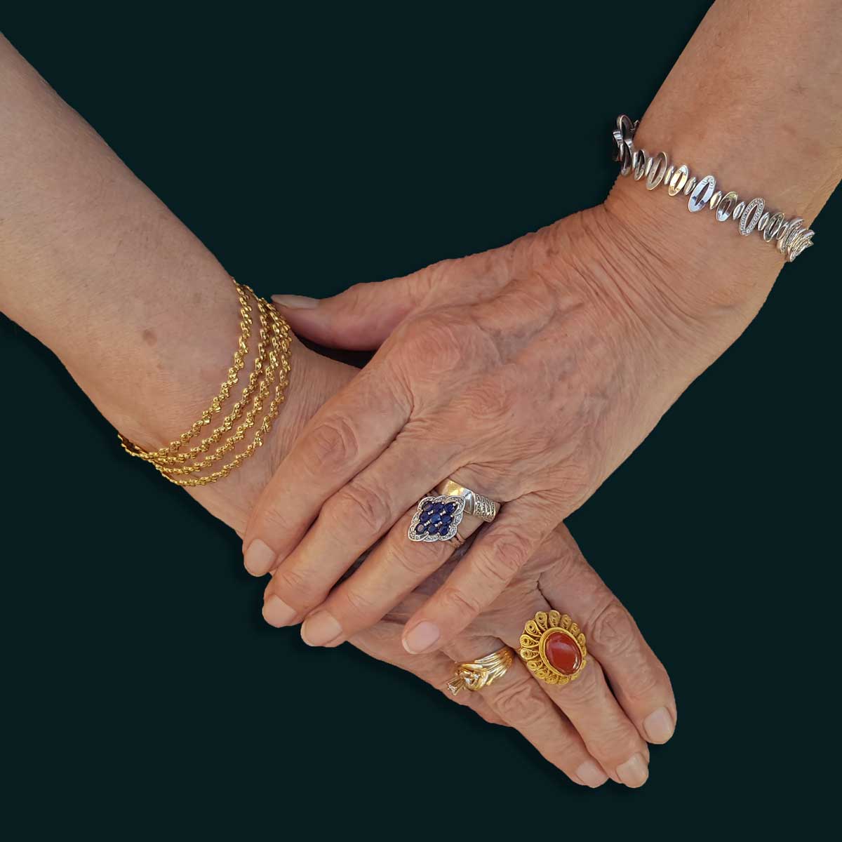 Elderly woman's hands clasped, with deep wrinkles and adorned with gold and gemstone jewelry
