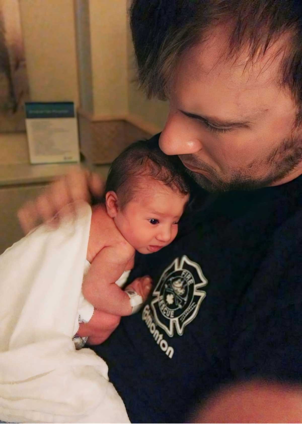 A close-up image of a father holding a naked and alert newborn infant to his chest.