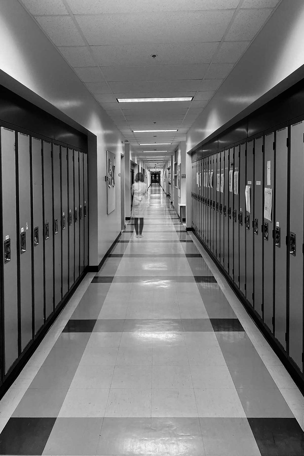 A female scientist is a long corridor from a university building. There are countless doors on either side.