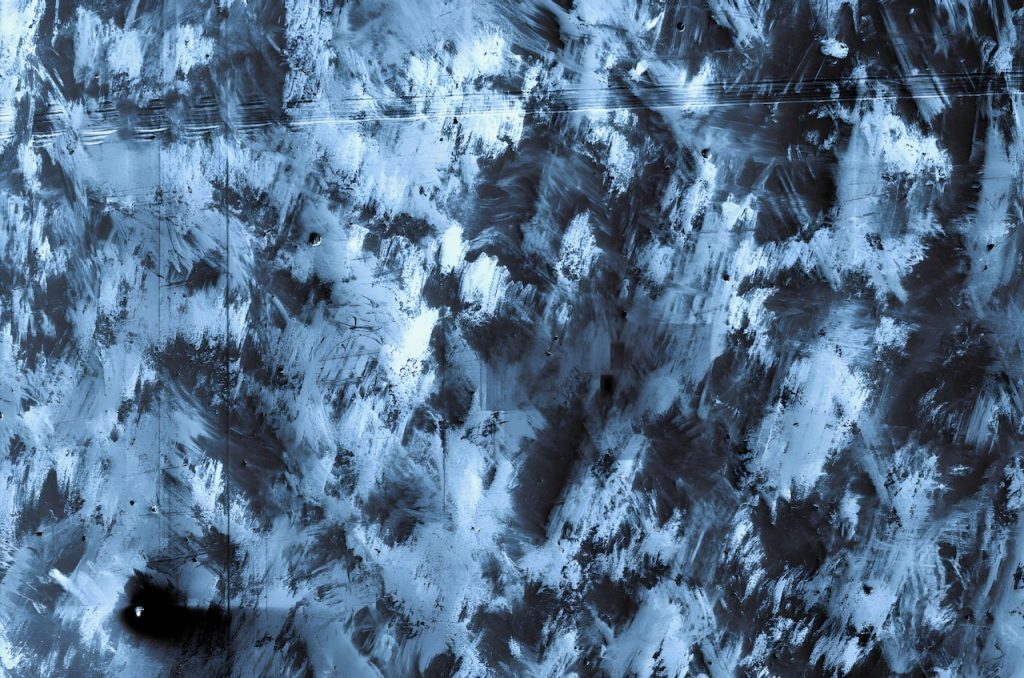 Magnified view of stainless steel surface showing abstract patterns of swirls and scratches from surface defects and contaminants.