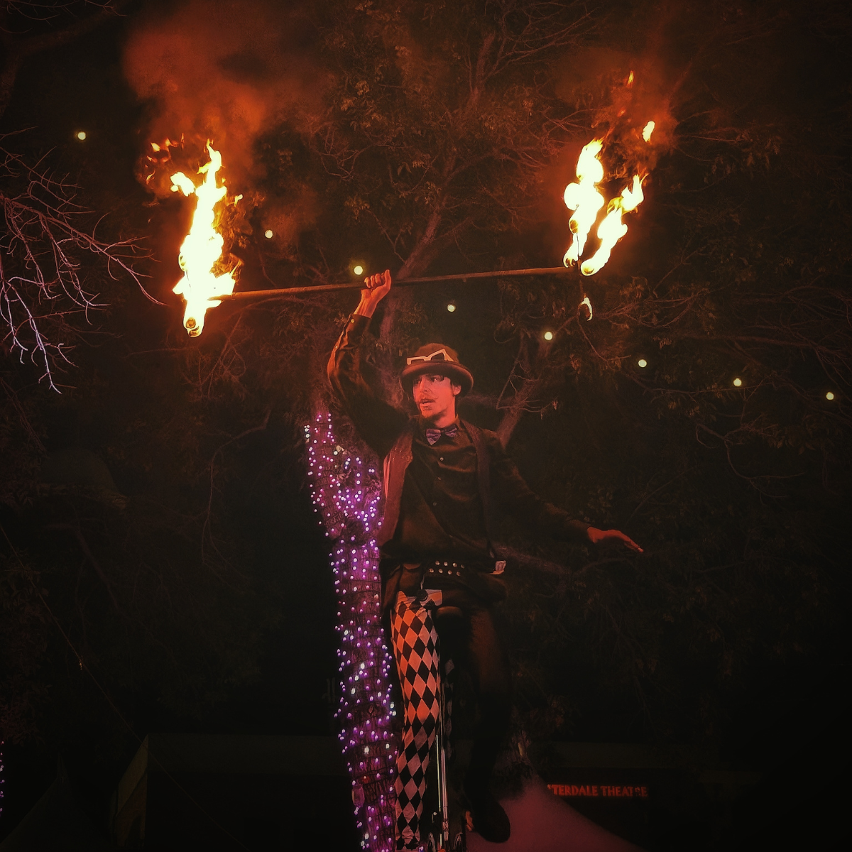 A street performer balances on a unicycle at night while holding a flaming staff.