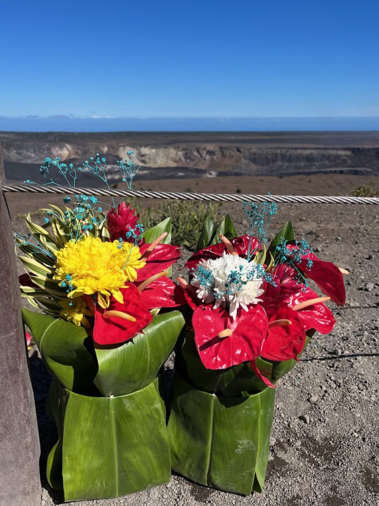 An offering of Native Hawaiian flowers wrapped in ti leaves placed on the ground near the rim of a volcanic caldera.