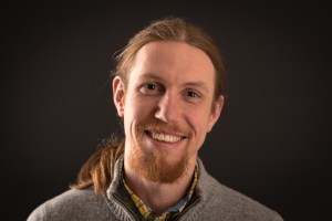 Head and shoulders image of Stephen Ullstrom, indexer, smiling at viewer. He is a young man with long reddish-brown hair in a ponytail.