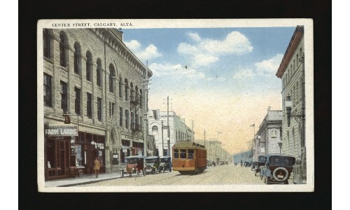 A street car travels down the middle of a street lined by buildings and early 1900s touring cars. Text at the top reads 'Center Street, Calgary, Alta.'