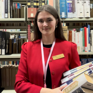 Abigail Deck holds books in her arms in the library stacks.